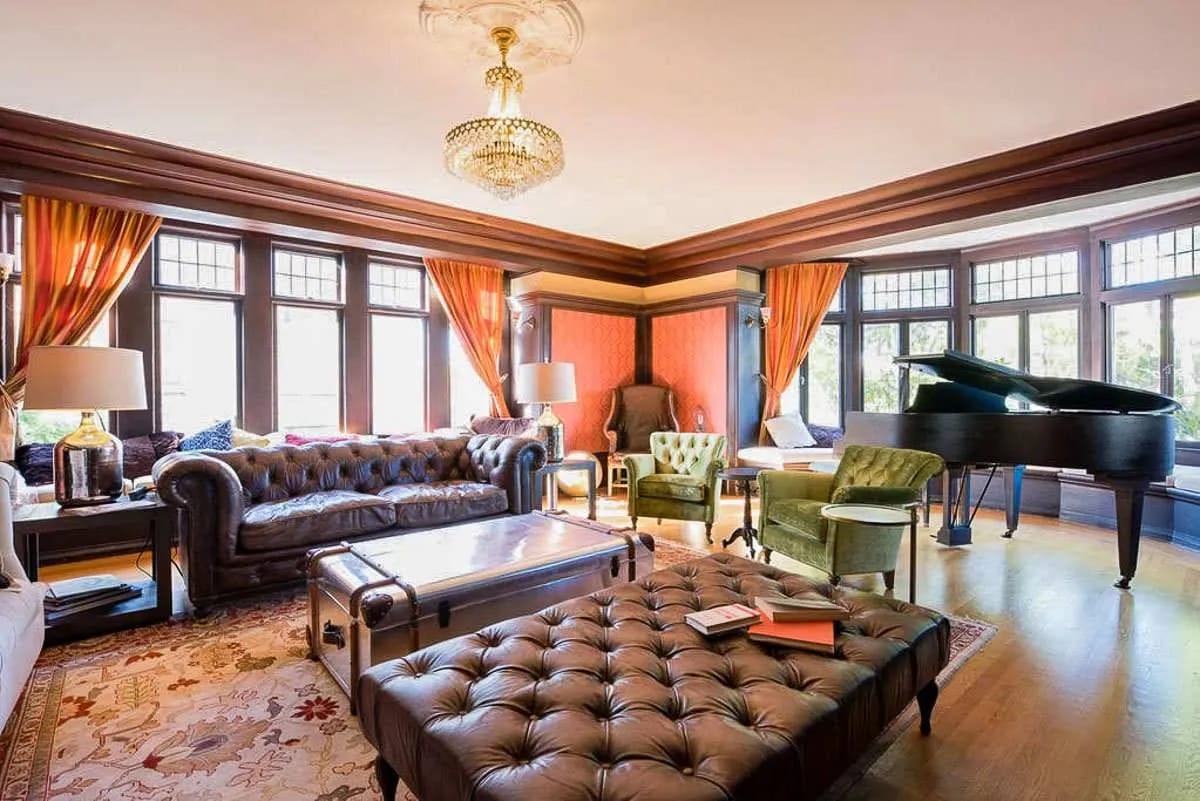 The Euclid Manor living room with chesterfield sofas, a grand piano, and a chandelier in afternoon light